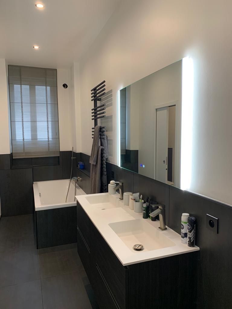 Salle de bain avec double vasque sur plan noir, miroir sur toute la longueur et douche vitrée