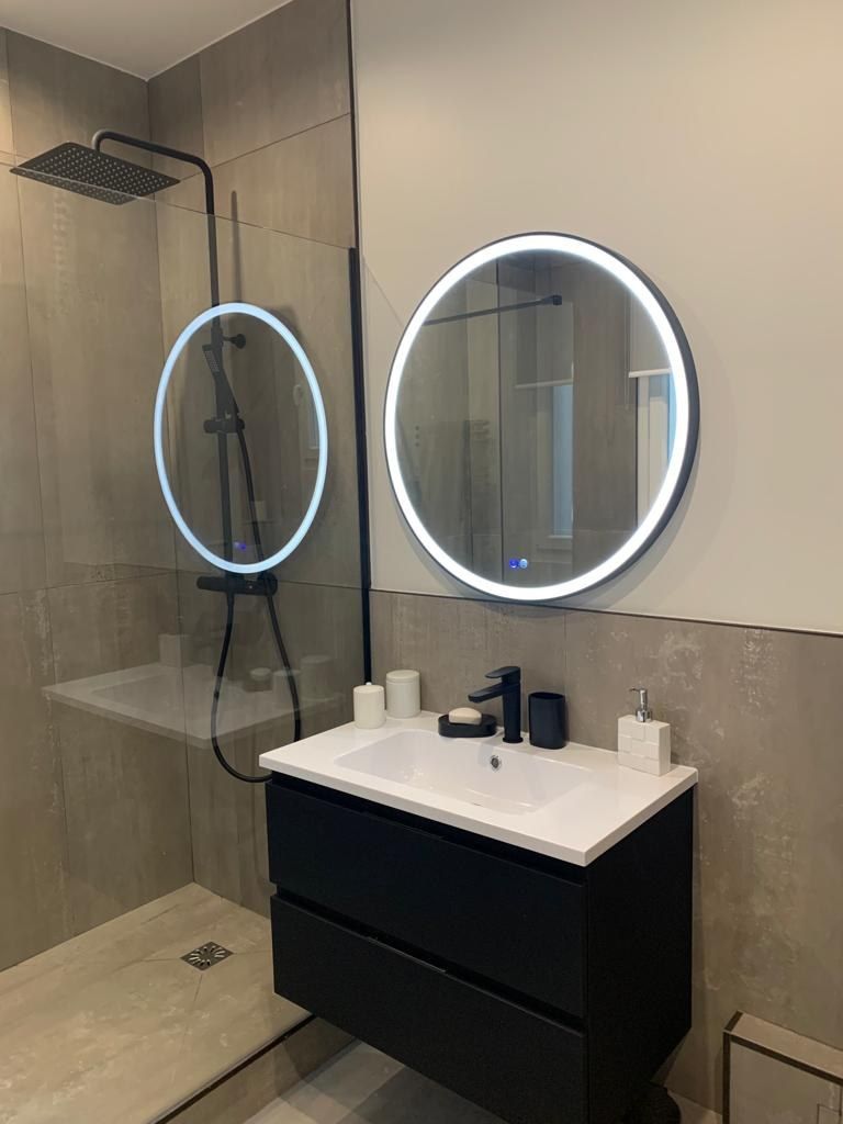 Salle de bain avec miroirs ronds rétroéclairés, meuble suspendu noir et paroi vitrée