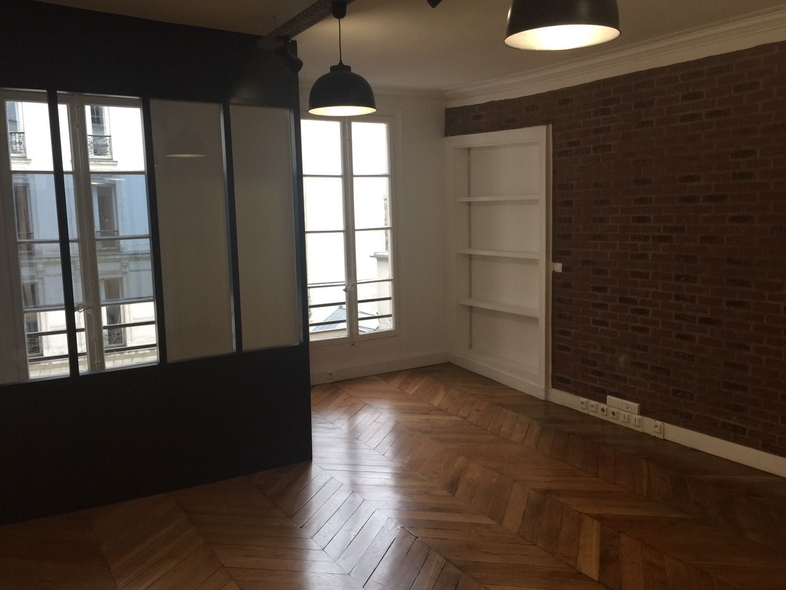 Séjour ouvert avec parquet chevron rénové, mur de brique conservé et verrière atelier