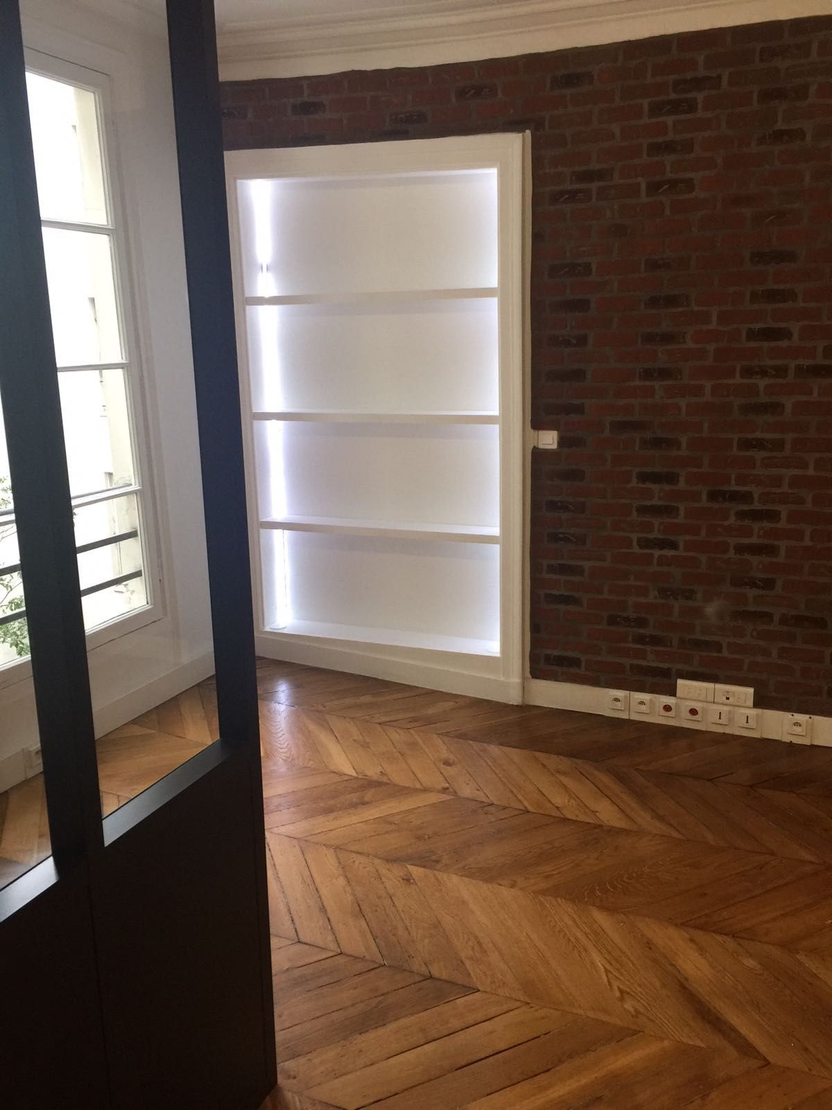 Verrière atelier en acier noir séparant deux pièces, sur parquet chevron rénové